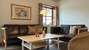 Een woonkamer met een zithoek, een salontafel, een lamp en een kunstwerk in een lijst aan de muur.