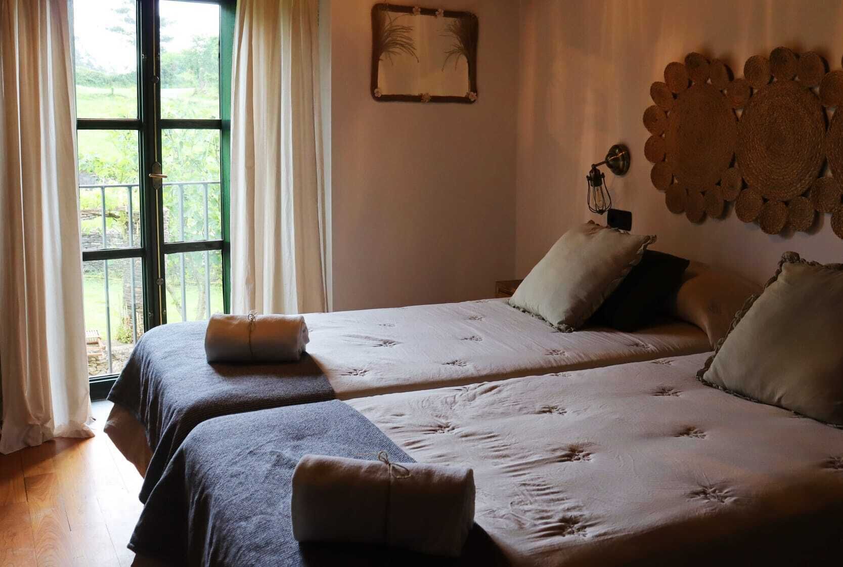 Un dormitorio con dos camas, una ventana con cortinas, una lámpara fijada a la pared y un adorno decorativo.