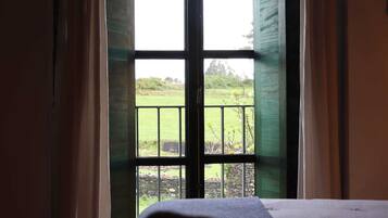 A room with a bed, a window with a view of a green landscape, and curtains.