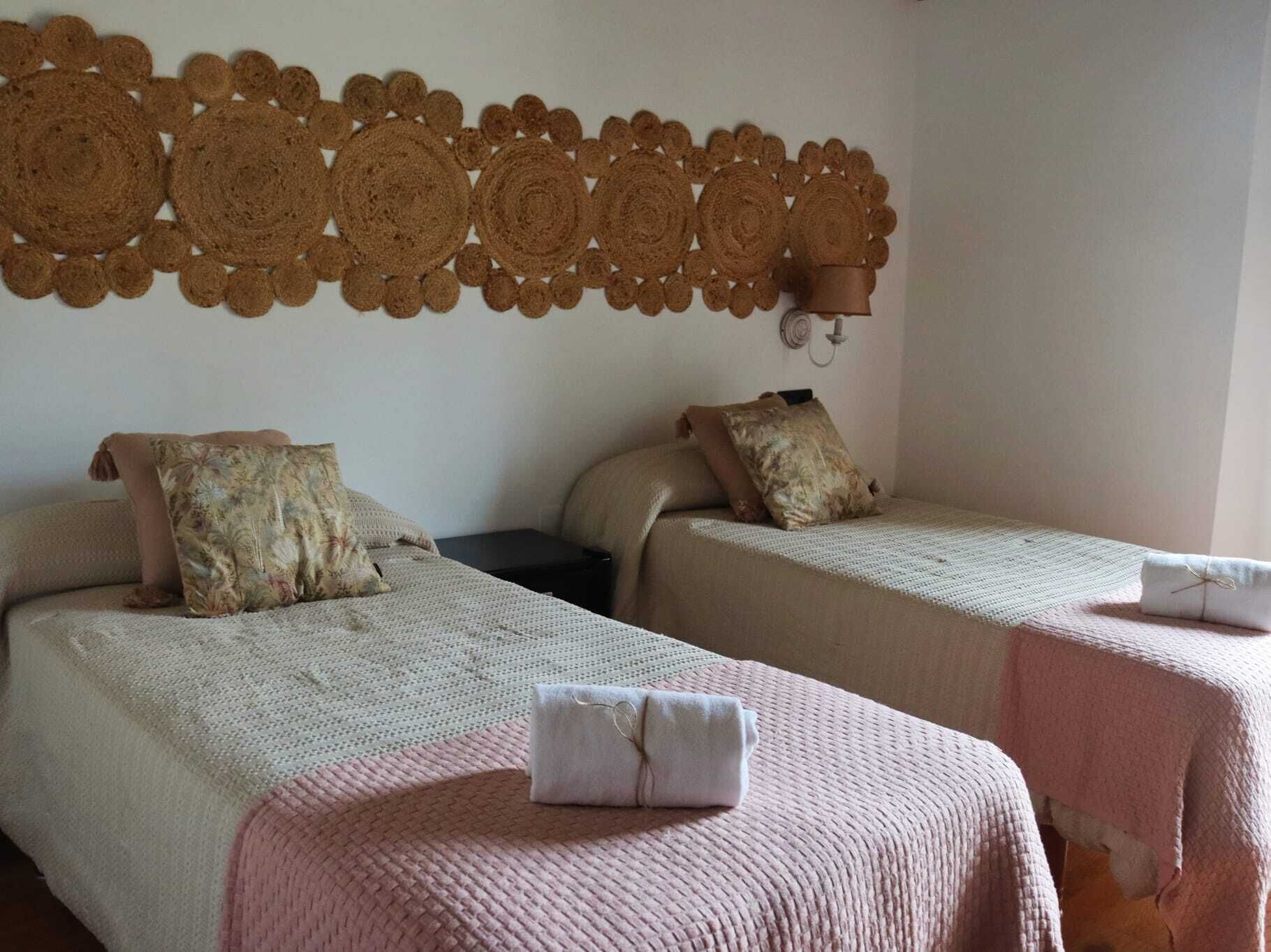 A hotel room with two beds, each with a pillow and a blanket. There is a wall decoration above the beds.