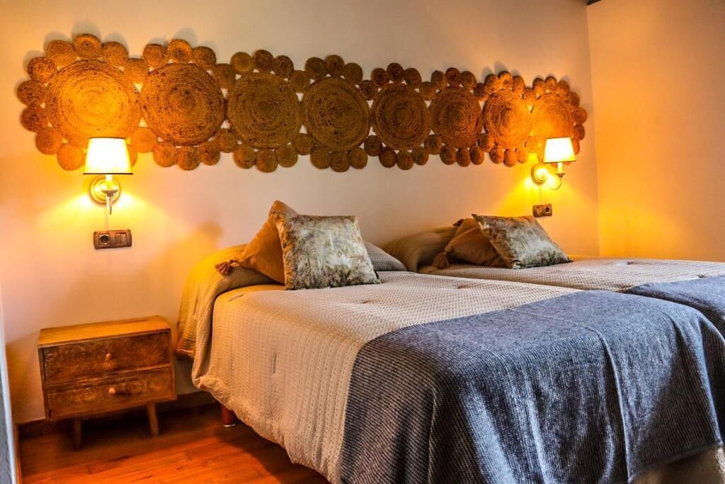 Un dormitorio con cama, almohadas, una mesita de noche y detalles decorativos en la pared.