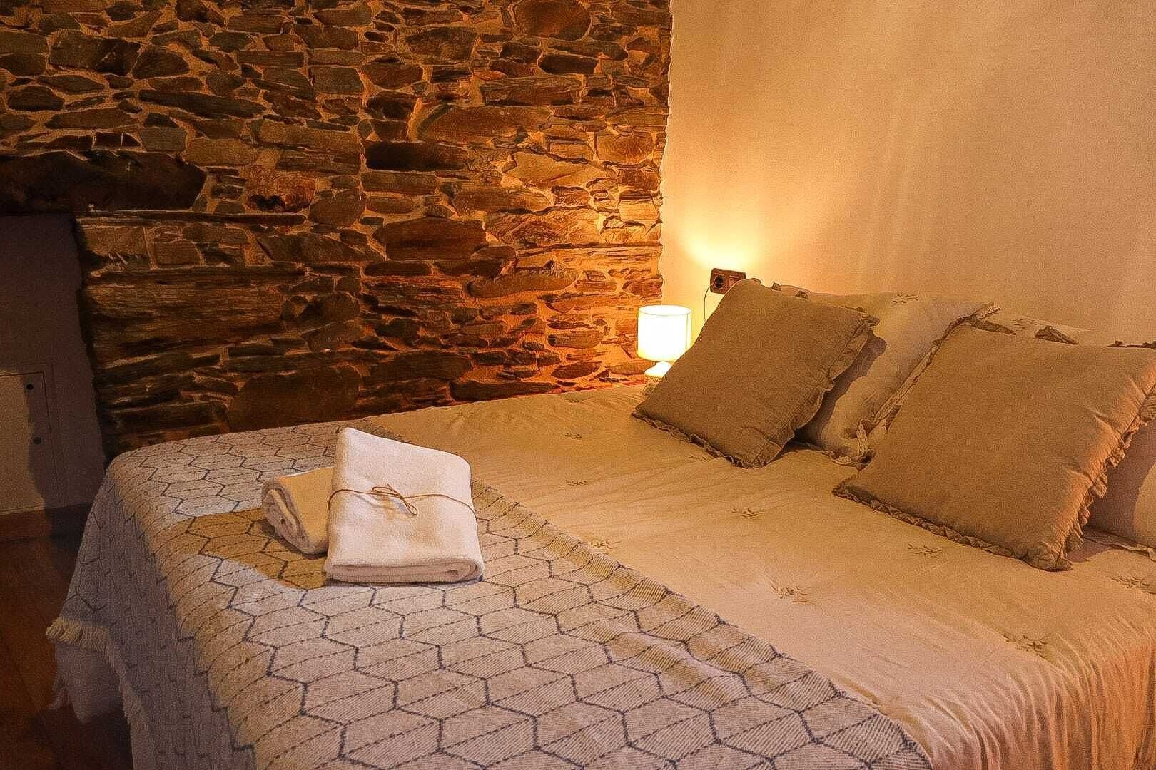 Een bed met een beddegoed met patroon, twee kussens en een opgevouwen handdoek.