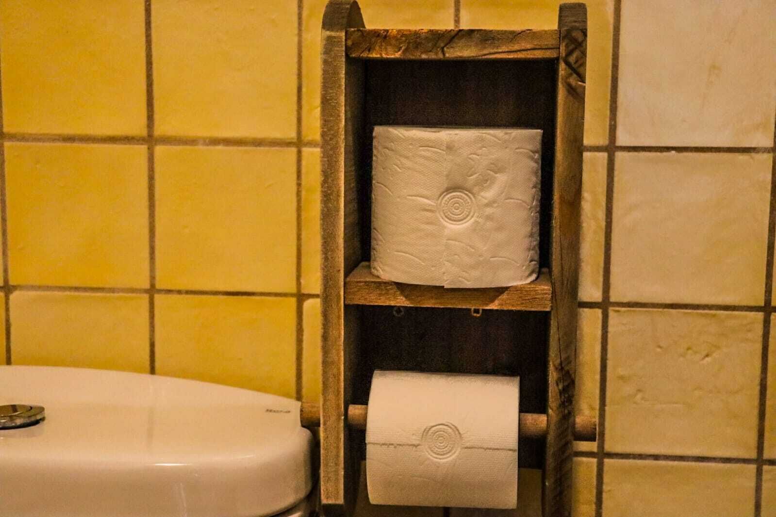 Ein Holzregal mit zwei Toilettenpapierrollen an einer gefliesten Wand.
