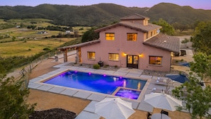 Uma casa de dois andares com piscina, área de estar ao ar livre e vista para as colinas ao redor.
