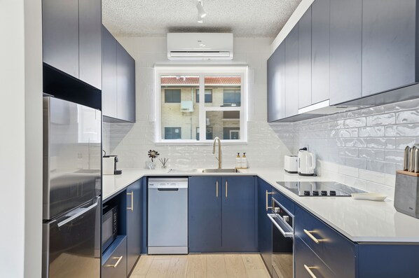 A modern kitchen with stainless steel appliances, a dishwasher, and a window with a view of buildings. - Belle Escapes - Coral Drift Retreat (West Beach)