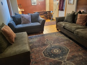 Un salon avec deux canapés, un tapis à motifs et une table à manger à l’arrière-plan.