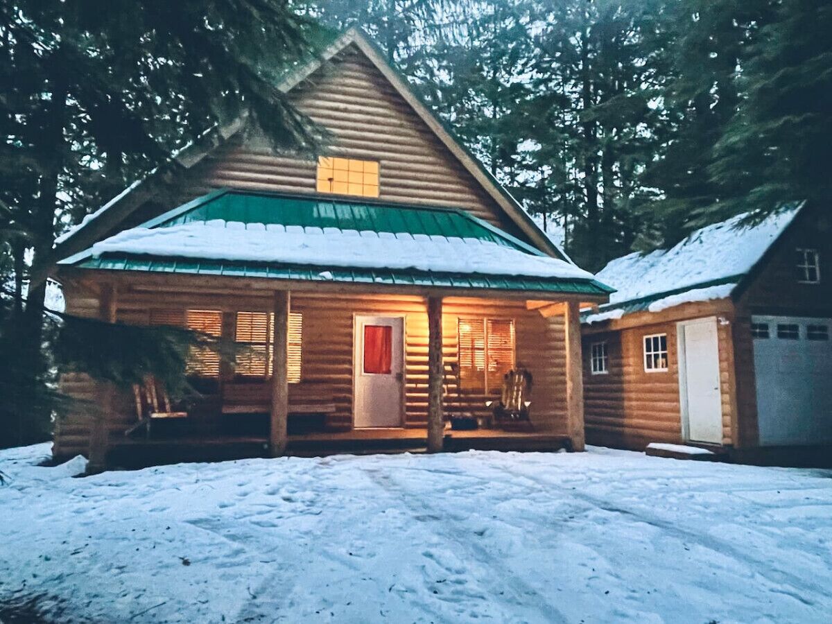 A log cabin with a green roof, a porch, and a garage.