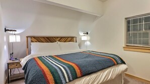 En snyggt bäddad säng med ett randigt överkast, en sänggavel i trä och två sänglampor.