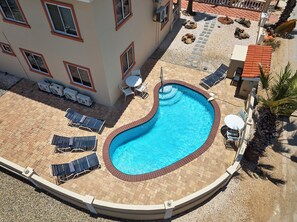 A swimming pool with sun loungers and a small table, surrounded by a brick patio and a building with multiple windows. - Aruba Oasis with pool, walking distance to the beach, hotels and restaurants (Palm Beach)