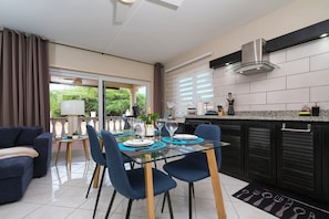 Een moderne keuken met een eethoek, met een glazen tafel, blauwe stoelen en uitzicht op groen.