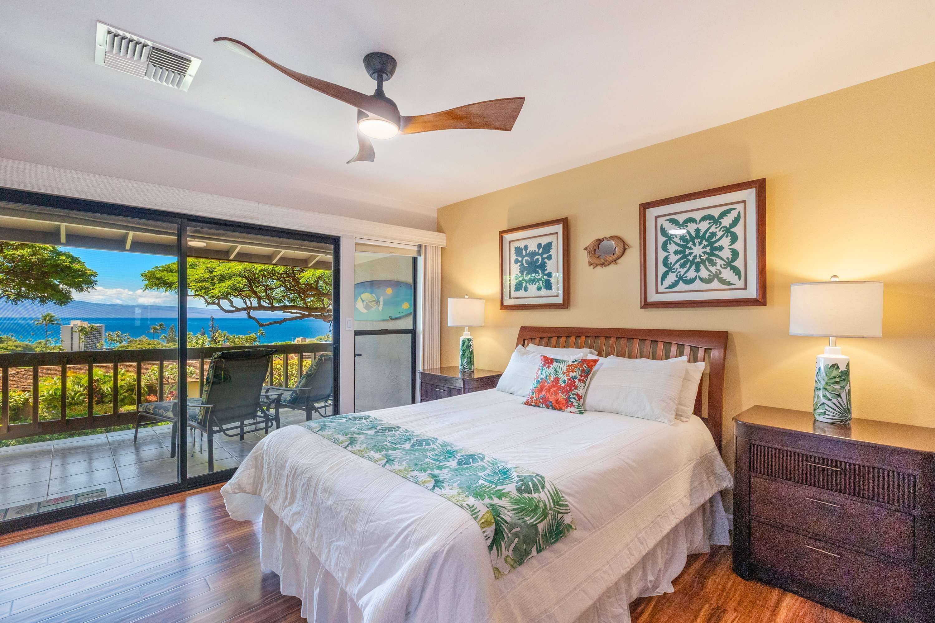 A bedroom with a bed, a nightstand, a ceiling fan, and a view of the ocean through a sliding door.