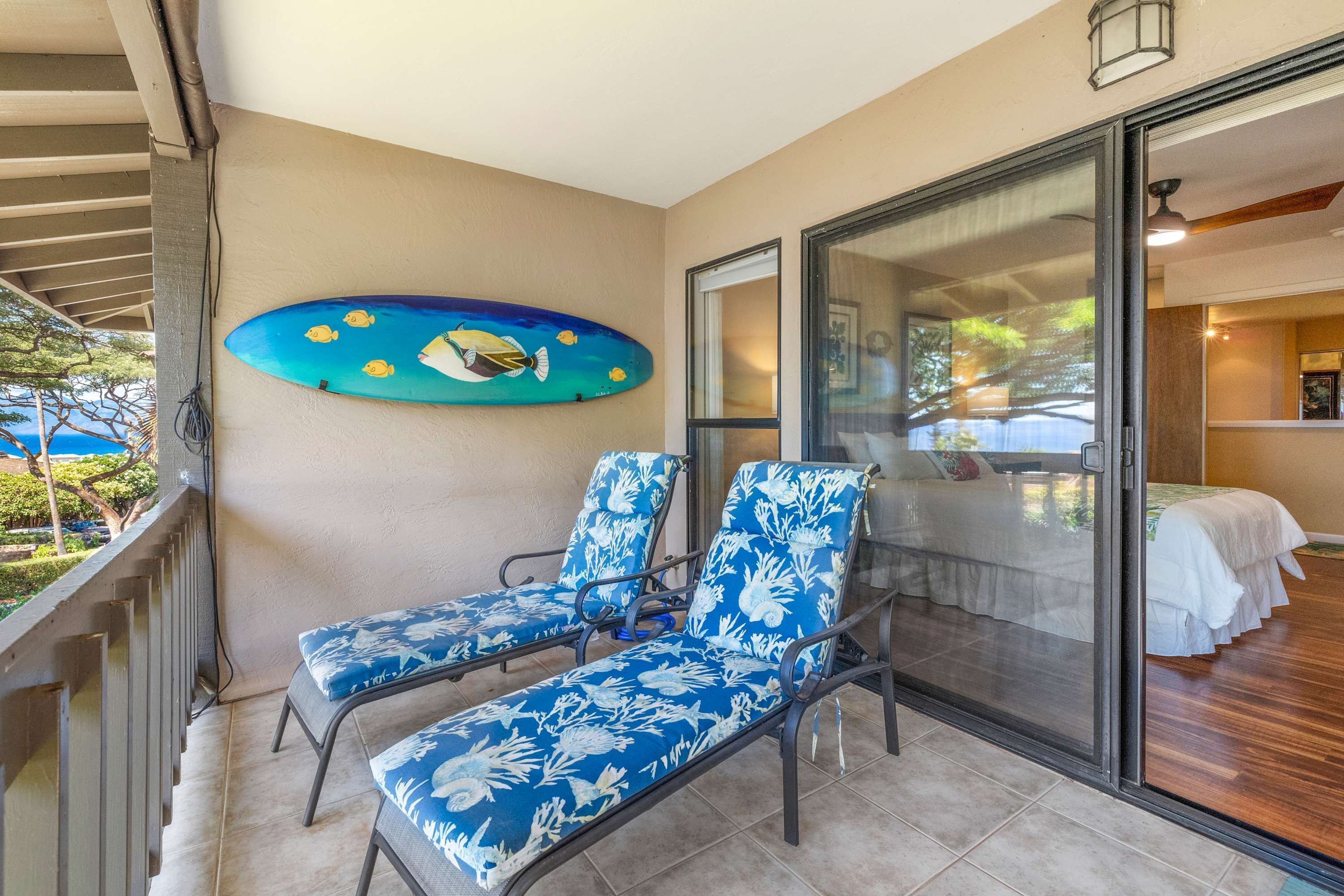 Ein Balkon mit zwei Liegestühlen, einer Glastür, die zu einem Schlafzimmer führt, und einem an der Wand befestigten Surfbrett.