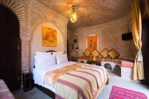 Una habitación con cama, una mesita, televisor montado en la pared y un arco decorativo.