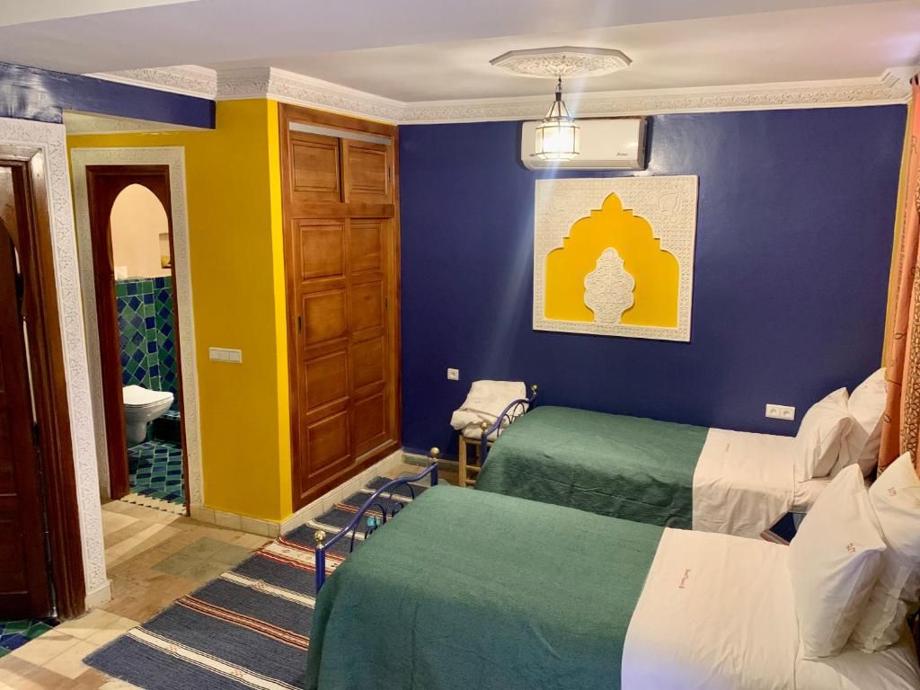 Quarto com duas camas, guarda-roupa de madeira, banheiro com parede azulejada em azul e verde, e um objeto decorativo na parede.