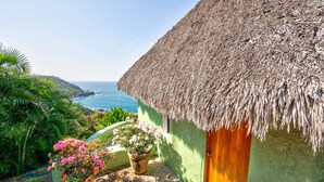A thatched-roof house with a view of the sea, surrounded by lush greenery and potted flowers. - Careyes (Costa Careyes)