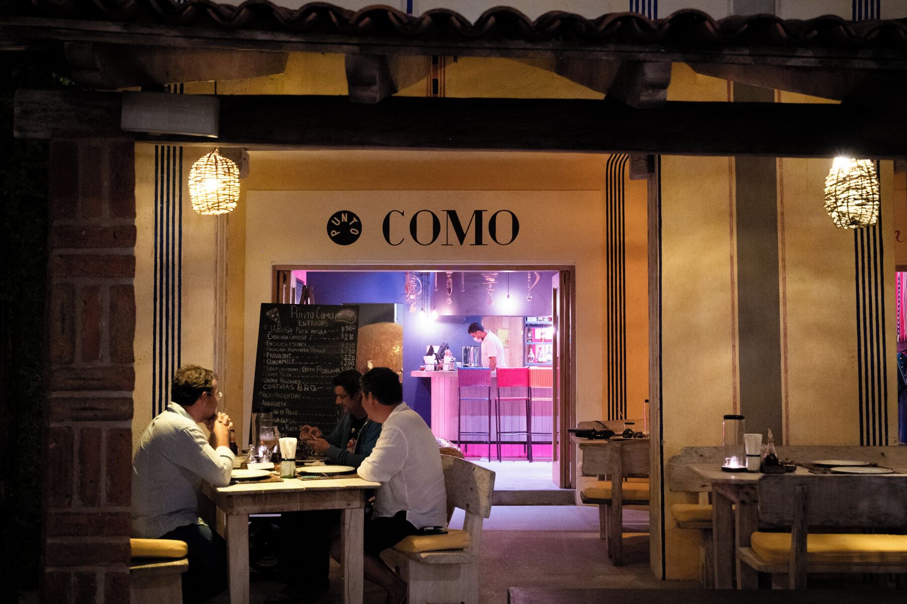 Un restaurante acogedor llamado "COMO" con un menú en la pizarra, muebles de madera y un ambiente cálido.