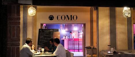 Un restaurante acogedor llamado "COMO" con un menú en la pizarra, muebles de madera y un ambiente cálido.