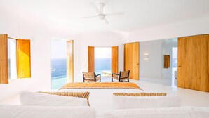 A spacious bedroom with a large bed, two chairs, and a view of the ocean. - Careyes (Costa Careyes)