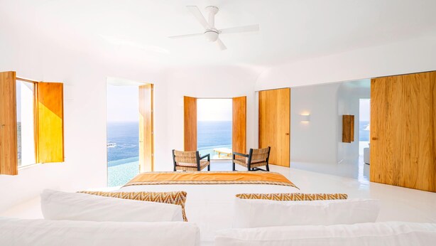 A spacious bedroom with a large bed, two chairs, and a view of the ocean.