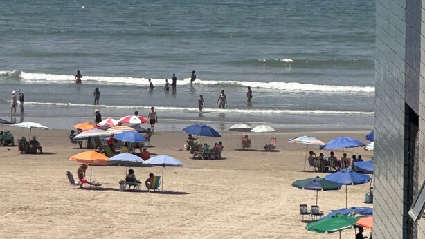 A beach with umbrellas and people, a boat in the water, and a building in the foreground. - Vacation/Carnival - SEA VIEW 3 Bedrooms - Sleeps 10! (Praia Grande)