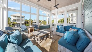 A covered outdoor living area with a wooden ceiling, large windows, and a blue sofa with matching cushions. - Blue Palmetto: Grayton Beach Retreat With Pool, Elevator, and 6-Passenger Electric Cart (Santa Rosa Beach)