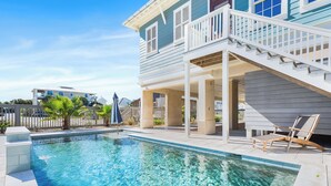 A swimming pool with a covered patio area, a staircase leading to a deck, and a view of neighboring houses. - Blue Palmetto: Grayton Beach Retreat With Pool, Elevator, and 6-Passenger Electric Cart (Santa Rosa Beach)