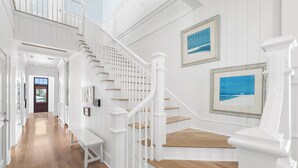 A spacious hallway with a wooden floor, white walls, and a white staircase with wooden steps. - Blue Palmetto: Grayton Beach Retreat With Pool, Elevator, and 6-Passenger Electric Cart (Santa Rosa Beach)