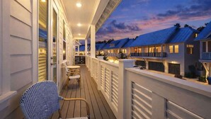 Un espace extérieur abrité doté d’une terrasse en bois, d’une rambarde blanche et d’une vue sur les bâtiments adjacents.