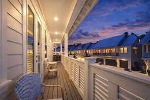 Ein überdachter Außenbereich mit Holzdeck, weißer Geländer und Blick auf angrenzende Gebäude.