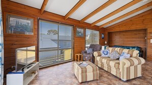 A cozy cabin interior with wooden walls, a sofa set, a small table, and a TV on a stand. - Neptune's Nook - Cape Paterson (Cape Paterson)