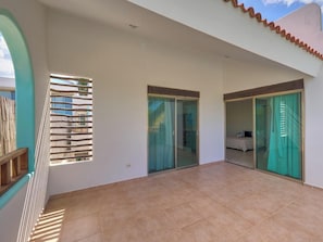 A spacious balcony with a tiled floor, a wooden staircase, and glass sliding doors leading to a bedroom. - Casa de Mormor  - Yucatan Home Rentals (Chicxulub Puerto)