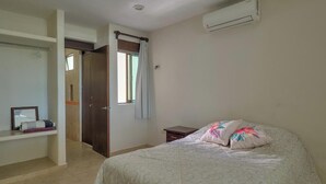 Een slaapkamer met een bed, een kledingkast, een nachtkastje en een airconditioning.