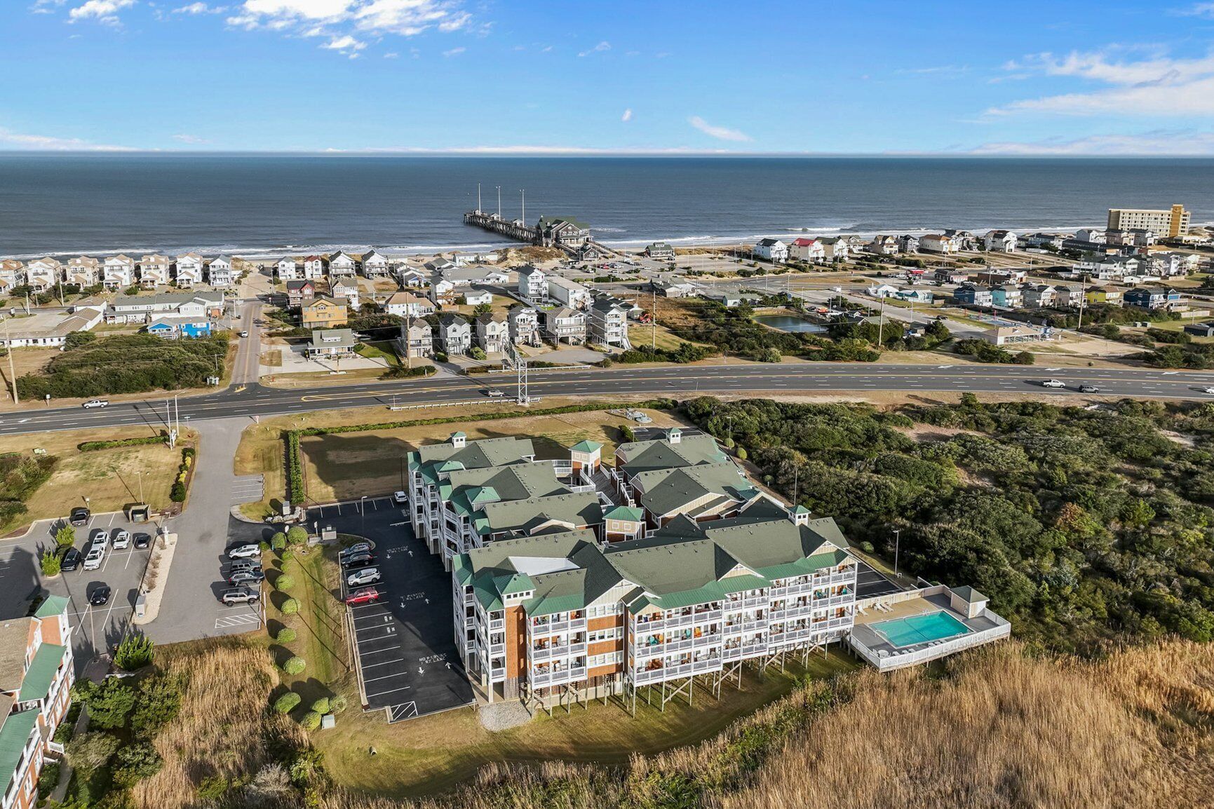 A coastal hotel with multiple floors, a parking lot, and a view of the ocean.