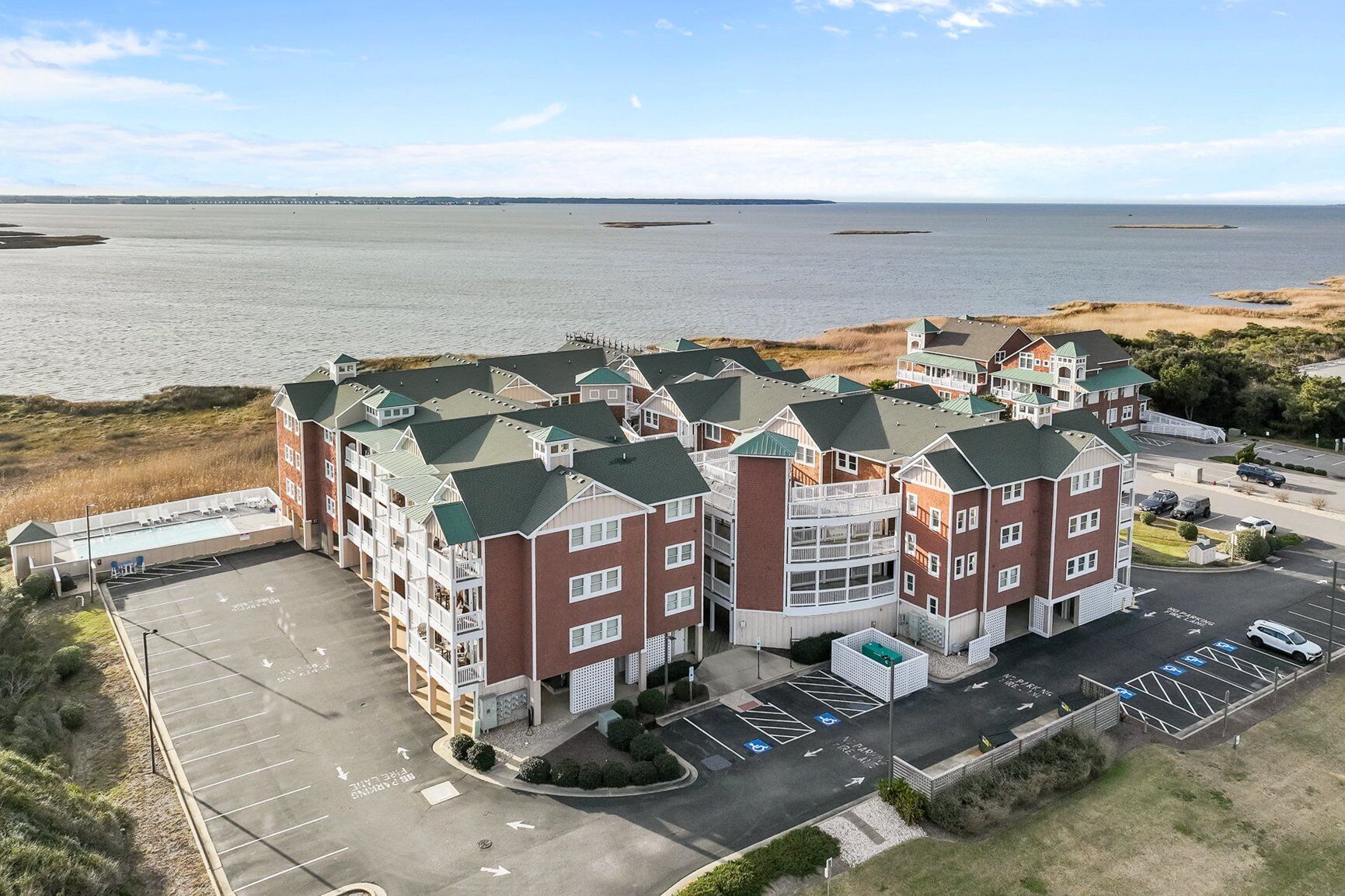A multi-story hotel with a parking lot and a view of the sea.