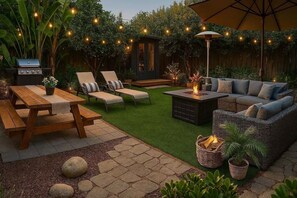 Un patio trasero con una mesa de madera, sillas de lounge, un pozo de fuego y un sofá.