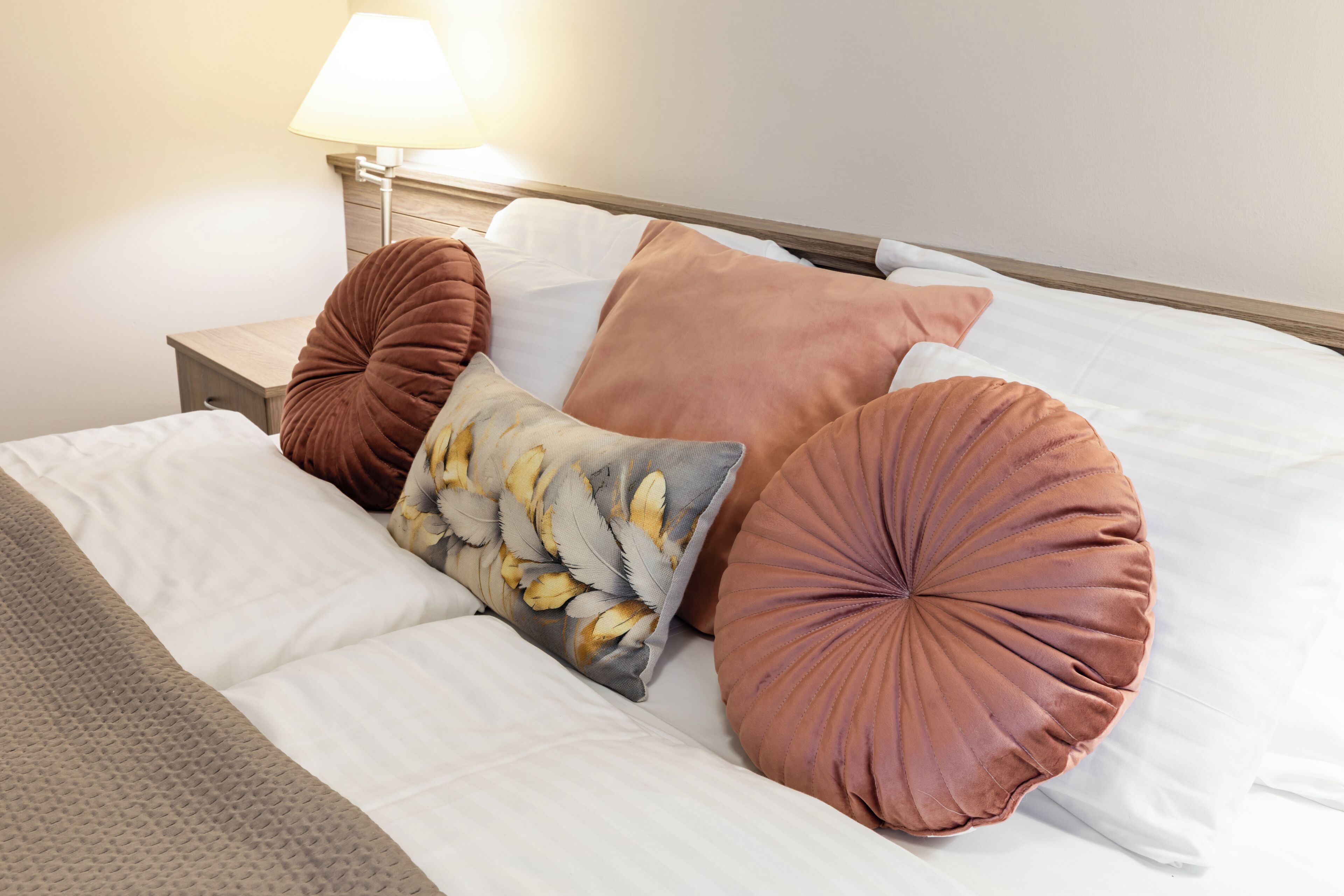 A neatly made bed with white linens, multiple pillows, and a lamp on a bedside table.