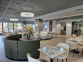 Un comedor moderno con mesas redondas, asientos acolchados y una planta decorativa en el centro.