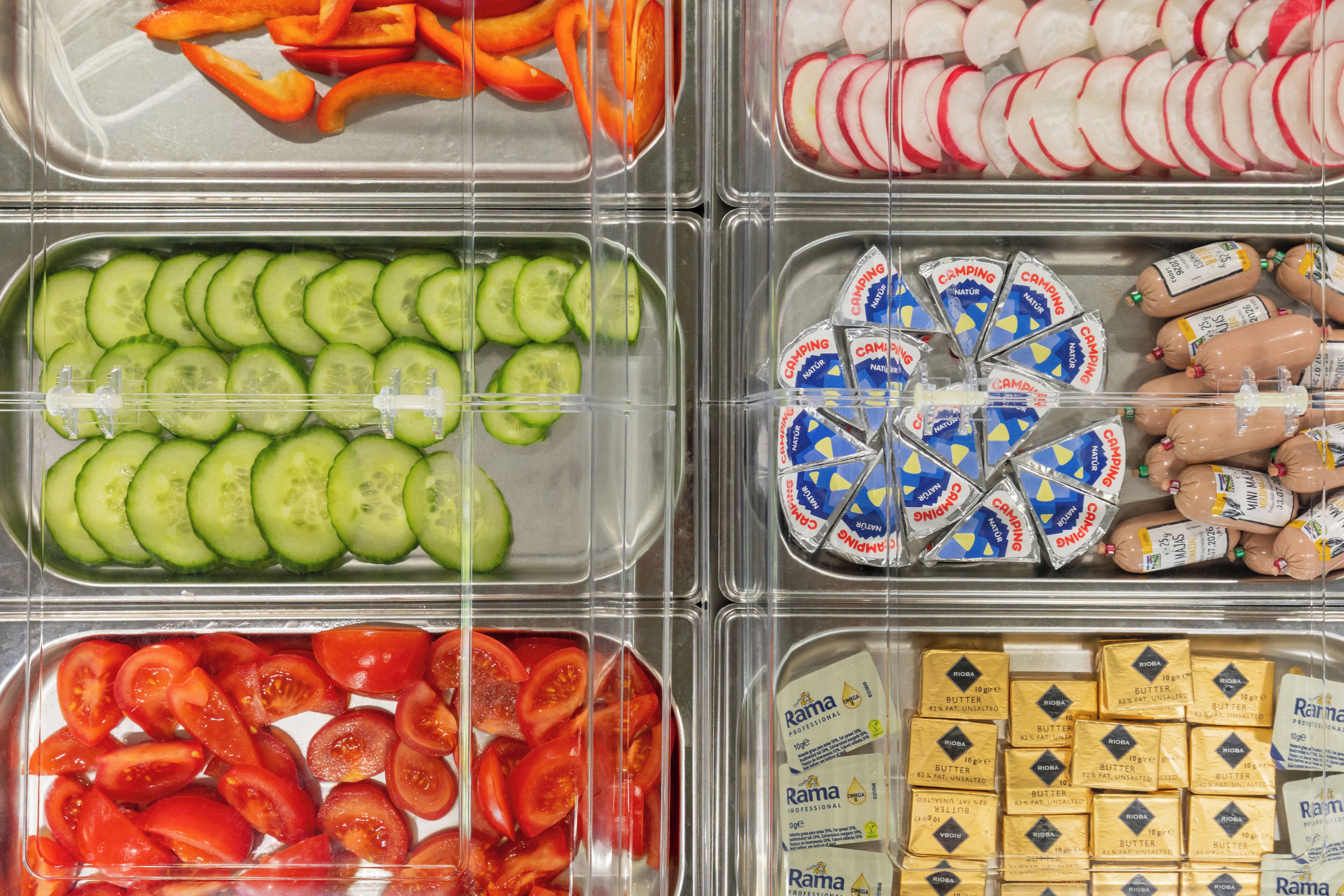 A food display with various items including sliced cucumbers, tomatoes, radishes, and packaged sausages.