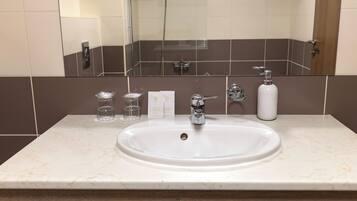 Un baño con lavamanos blanco, un espejo y artículos de aseo en la encimera.