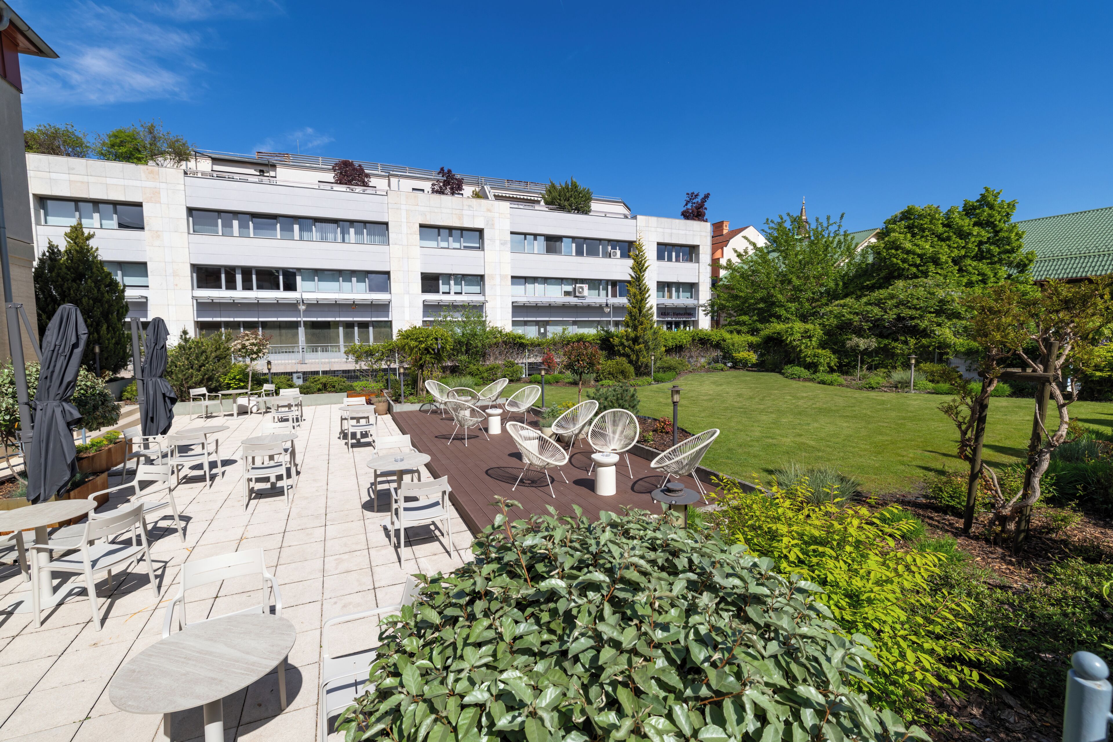 A hotel courtyard with outdoor seating, a well-maintained lawn, and a modern building in the background.