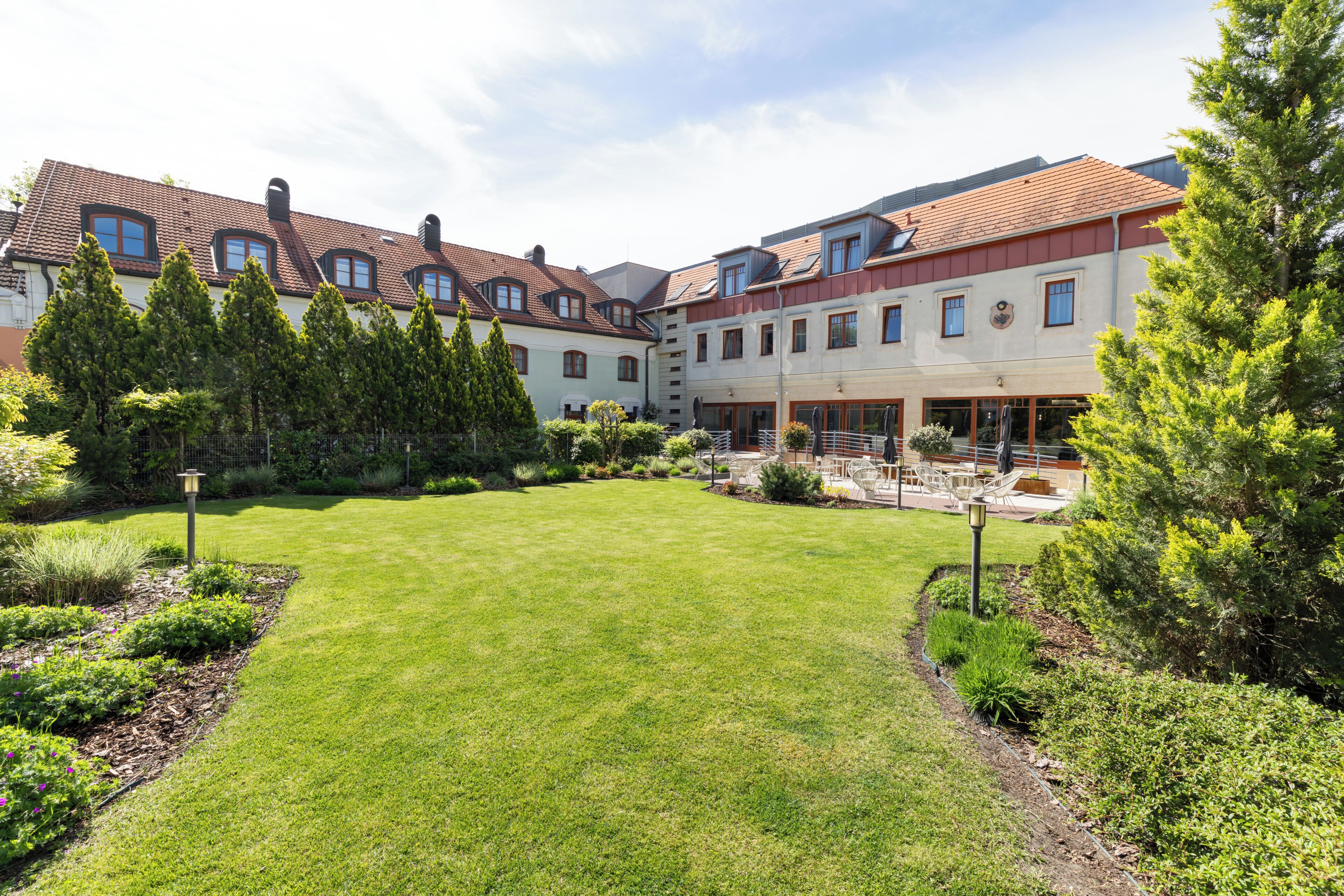 A courtyard with a lawn, surrounded by buildings with red-tiled roofs and multiple windows.