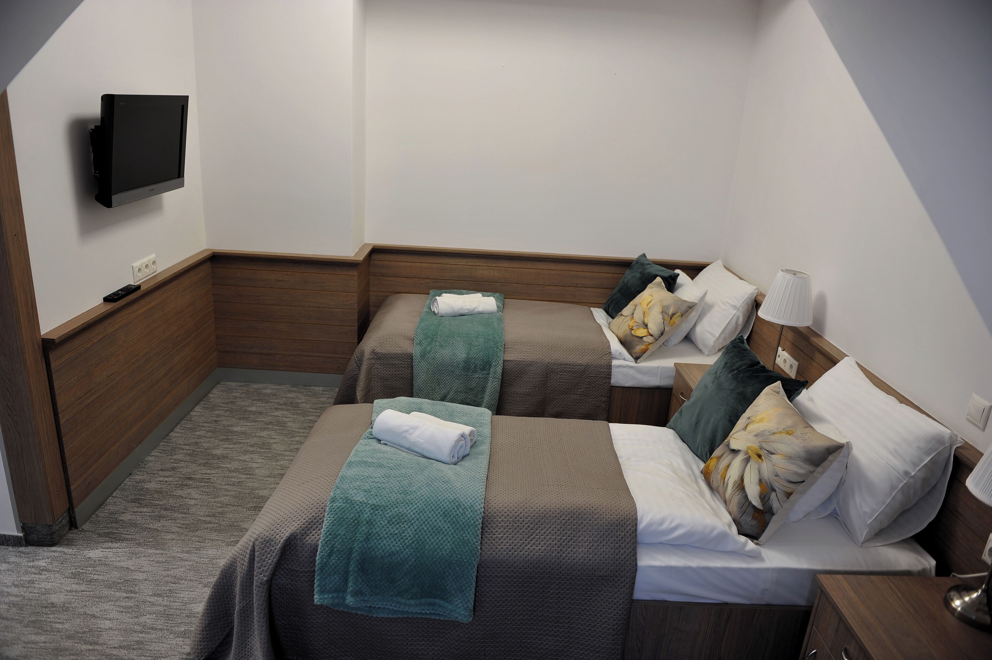 A hotel room with two beds, a TV mounted on the wall, and a bedside lamp.