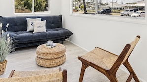 Uma sala de estar moderna com um sofá azul escuro, uma mesa de centro trançada e uma cadeira de madeira.