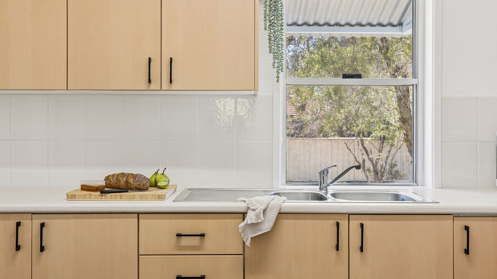 A kitchen with wooden cabinets, a window, and a countertop with a loaf of bread, a knife, and a pear.