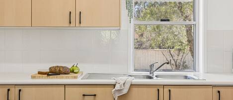 A kitchen with wooden cabinets, a window, and a countertop with a loaf of bread, a knife, and a pear.