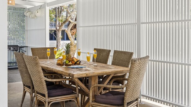 Uma mesa de madeira com cadeiras de vime, frutas e bebidas.
