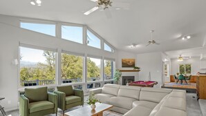 A spacious living room with large windows, a sectional sofa, a coffee table, and a pool table. - Sleeps 24 | Hot Tub | Firepit | 17 beds | 2 Houses (Oakhurst)