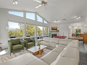 A spacious living room with large windows, a sectional sofa, a coffee table, and a pool table. - Sleeps 24 | Hot Tub | Firepit | 17 beds | 2 Houses (Oakhurst)