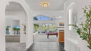 A spacious hallway with a pool table, a seating area, and large windows offering a view of the outdoors. - Sleeps 24 | Hot Tub | Firepit | 17 beds | 2 Houses (Oakhurst)