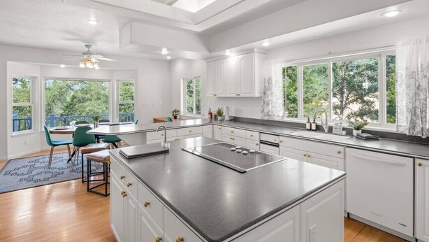 A modern kitchen with white cabinetry, a central island, and large windows offering a view of the outdoors. - Sleeps 24 | Hot Tub | Firepit | 17 beds | 2 Houses (Oakhurst)